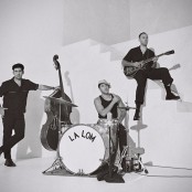 A black and white image of three men dressed in black by a staircase with instruments